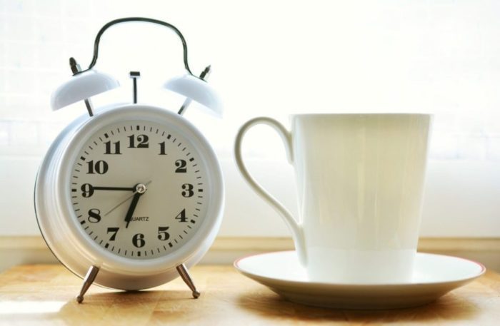 White alarm clock with cup of drink representing increased productivity with Ed Mylett 6 hour day technique