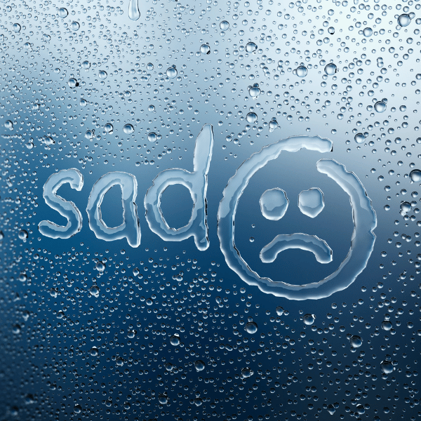 Rainy outside window with sad in small letters and sad face emoticon, representing negative emotional impact of nagative self talk