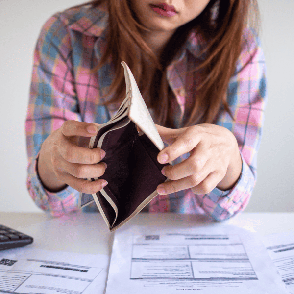 Woman showing an empty purse forward with papers scattered in front of her, showing she's broke and contemplating what to do