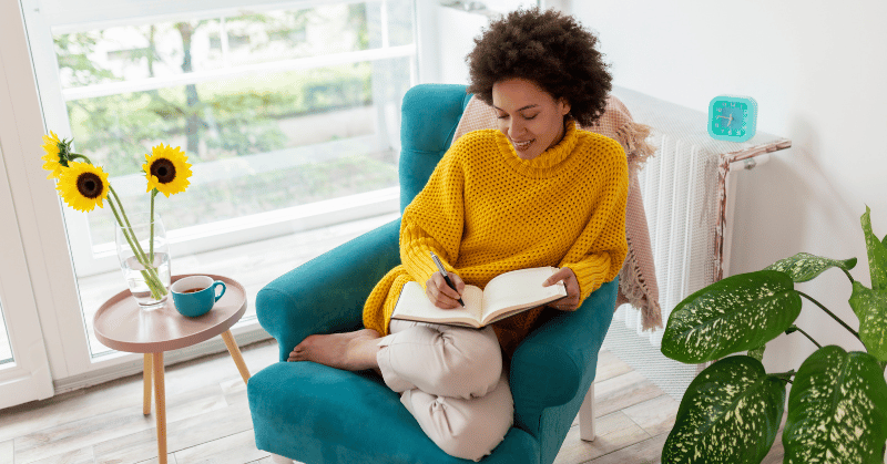 A woman sitting in an armchair, relaxing at home and writing a diary, symbolising implementing 30 day challenge ideas for personal reflection and writing