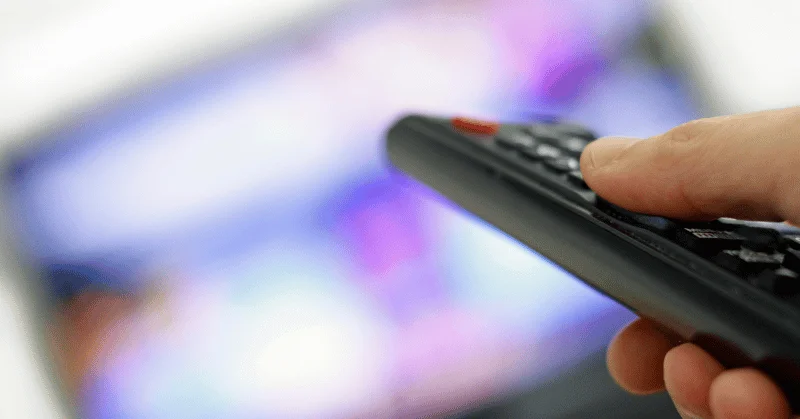 A remove control and blurred TV in the background demonstrating wasting time binge-watching TV