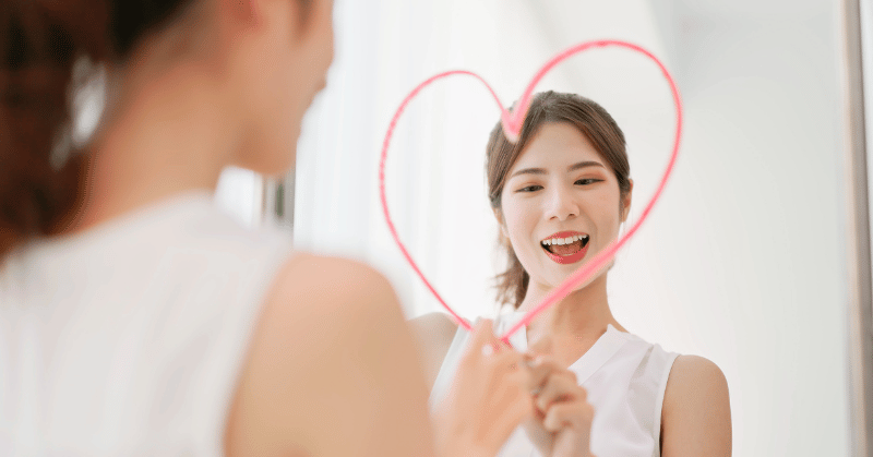 Woman drawing a heart shape on the mirror, symbolising positive self talk for self esteem