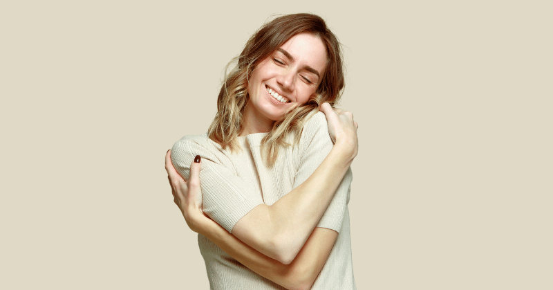 Woman embracing herself smiling, depicting the concept of positive self talk for self esteem