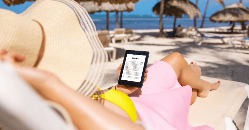 Woman on travel holding her Kindle reading on the beach, displaying no regret spending money