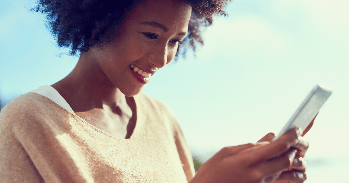 Woman looking at her phone smiling, demonstrating the effect of reading brighten your day quotes